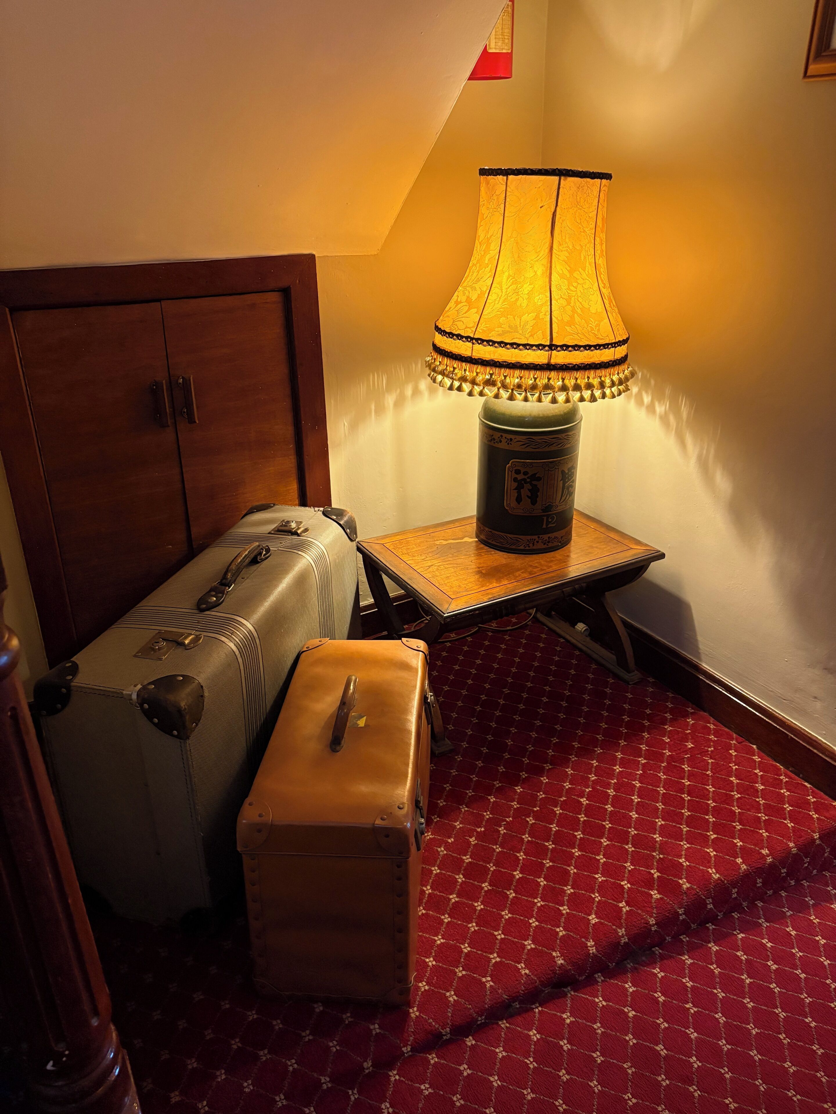 A room with a wooden cabinet, a table with a lamp, and two suitcases.