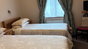 Habitación de hotel con dos camas, una ventana con cortinas, una mesita de noche, un televisor y un cuadro colgado en la pared.