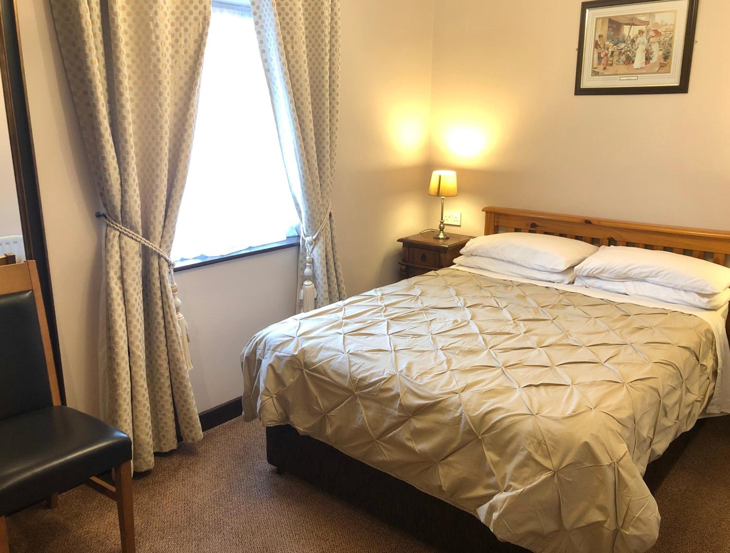Une chambre d’hôtel avec un lit, une chaise, une table de chevet avec une lampe et une fenêtre avec des rideaux.