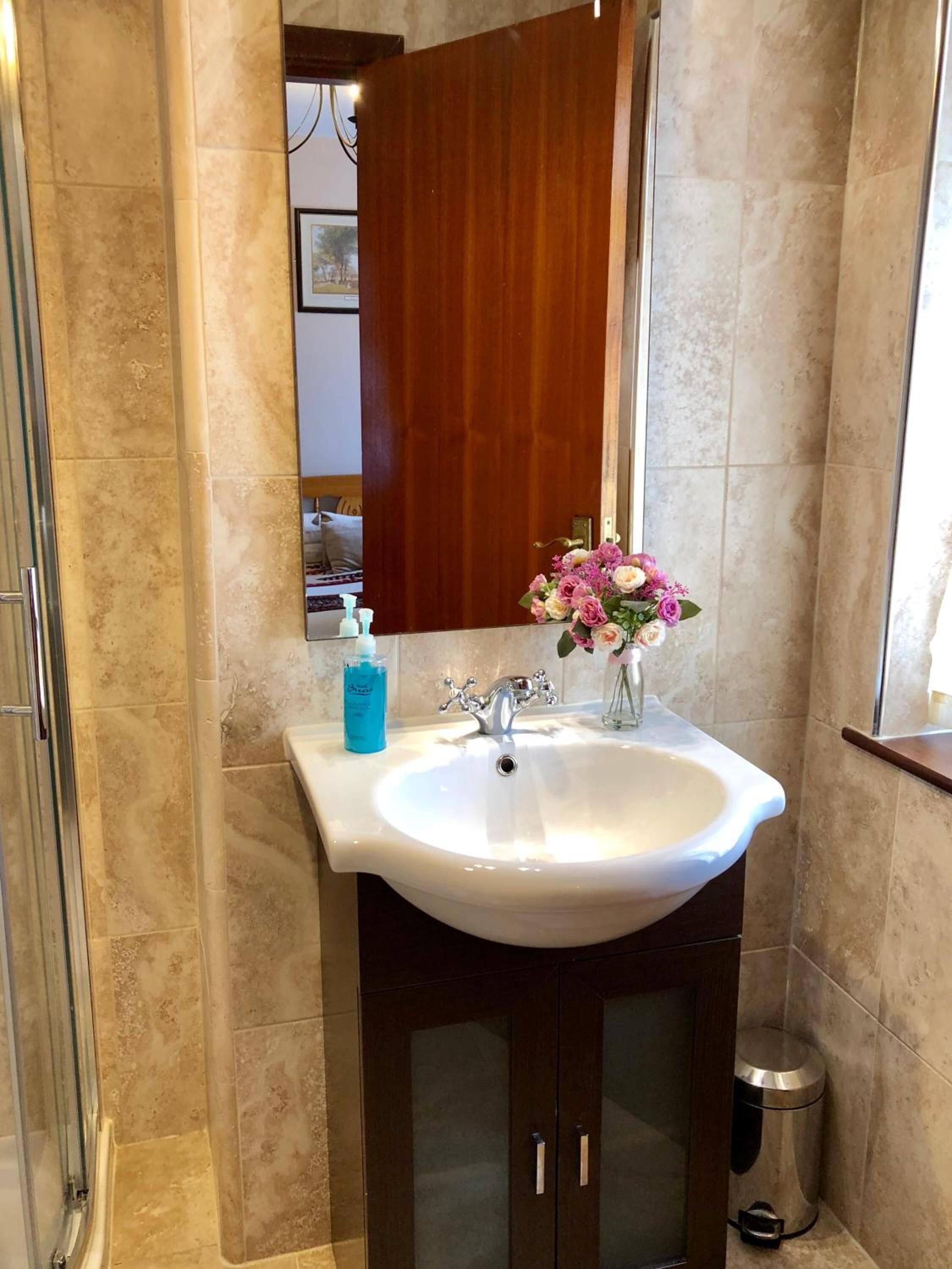 A bathroom with a white sink, a wooden cabinet, a mirror, and a trash can.