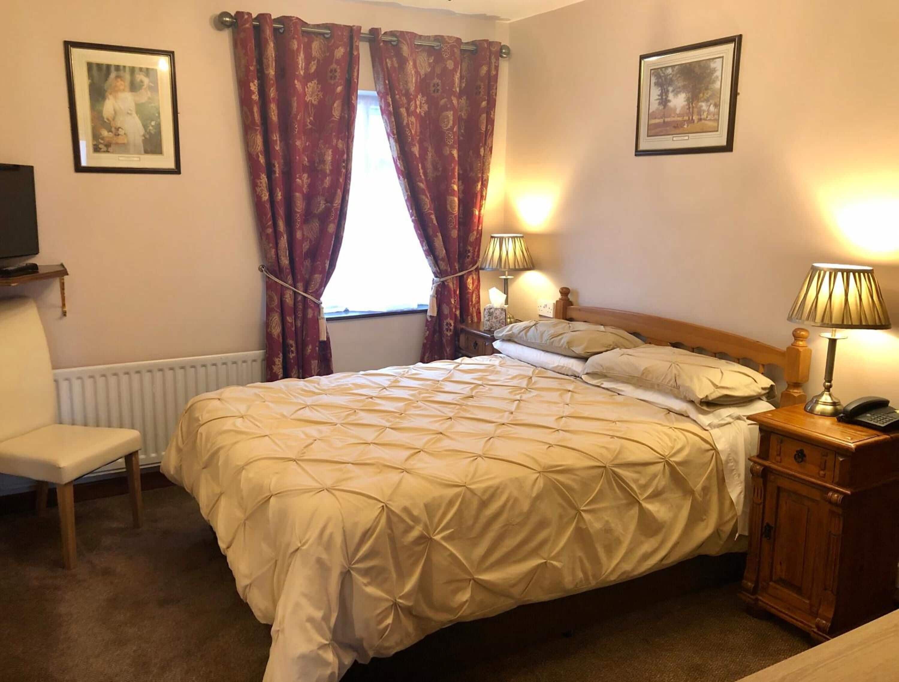 Une chambre d’hôtel avec un grand lit, deux lampes de chevet, une table de chevet en bois, une chaise et deux tableaux encadrés accrochés aux murs.