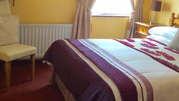 A hotel room with a bed, a chair, a nightstand, a lamp, and a television on a stand.