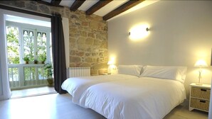 A bedroom with a large bed, stone wall, and a balcony with potted plants. - Artea Narrika (San Sebastián)
