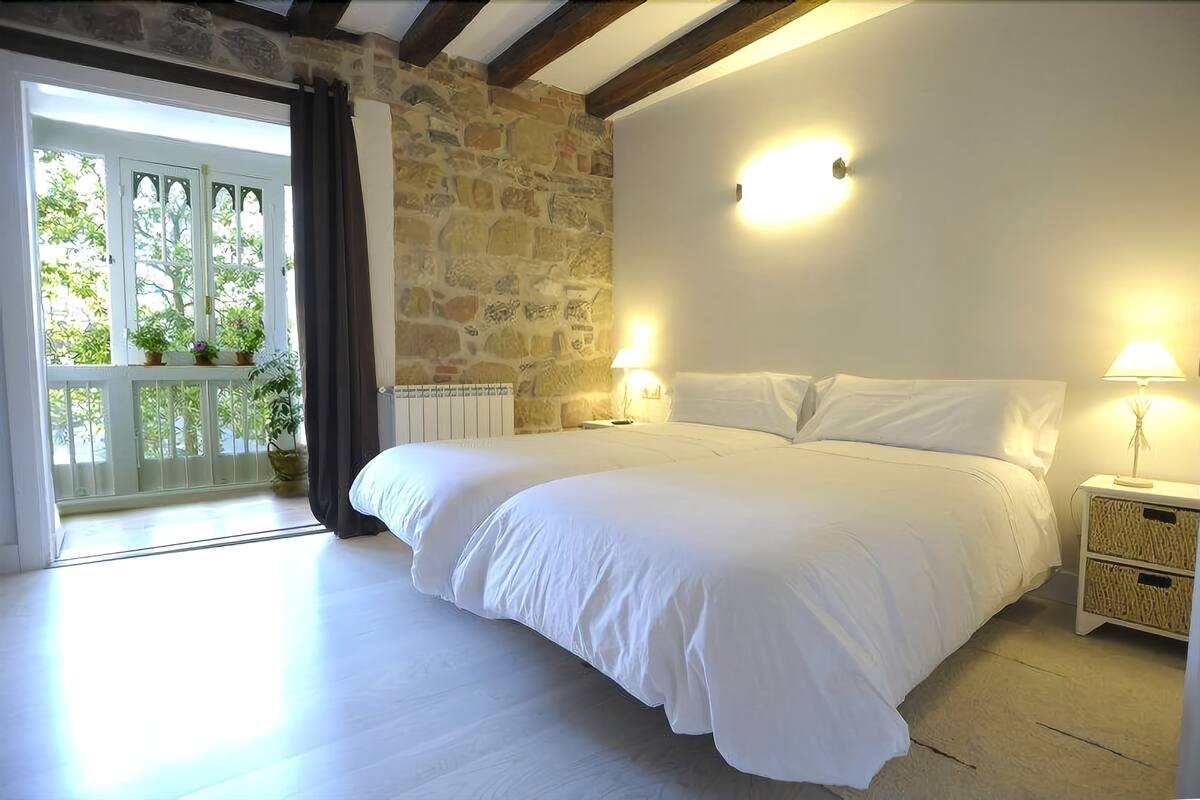 A bedroom with a large bed, stone wall, and a balcony with potted plants.