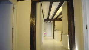 A hallway with exposed wooden beams and a white floor leading to a room with a white radiator. - Artea Narrika (San Sebastián)