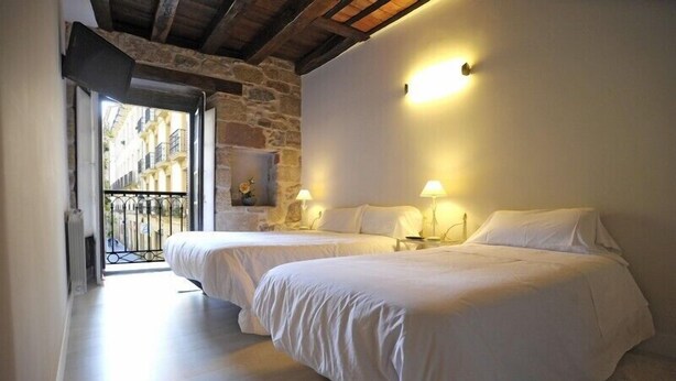 A bedroom with two beds, a stone wall, and a balcony with a metal railing. - Artea Narrika (San Sebastián)
