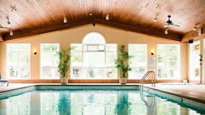 An indoor swimming pool with wooden ceiling beams, large windows, and potted plants. - Oakwood Resort (South Huron)