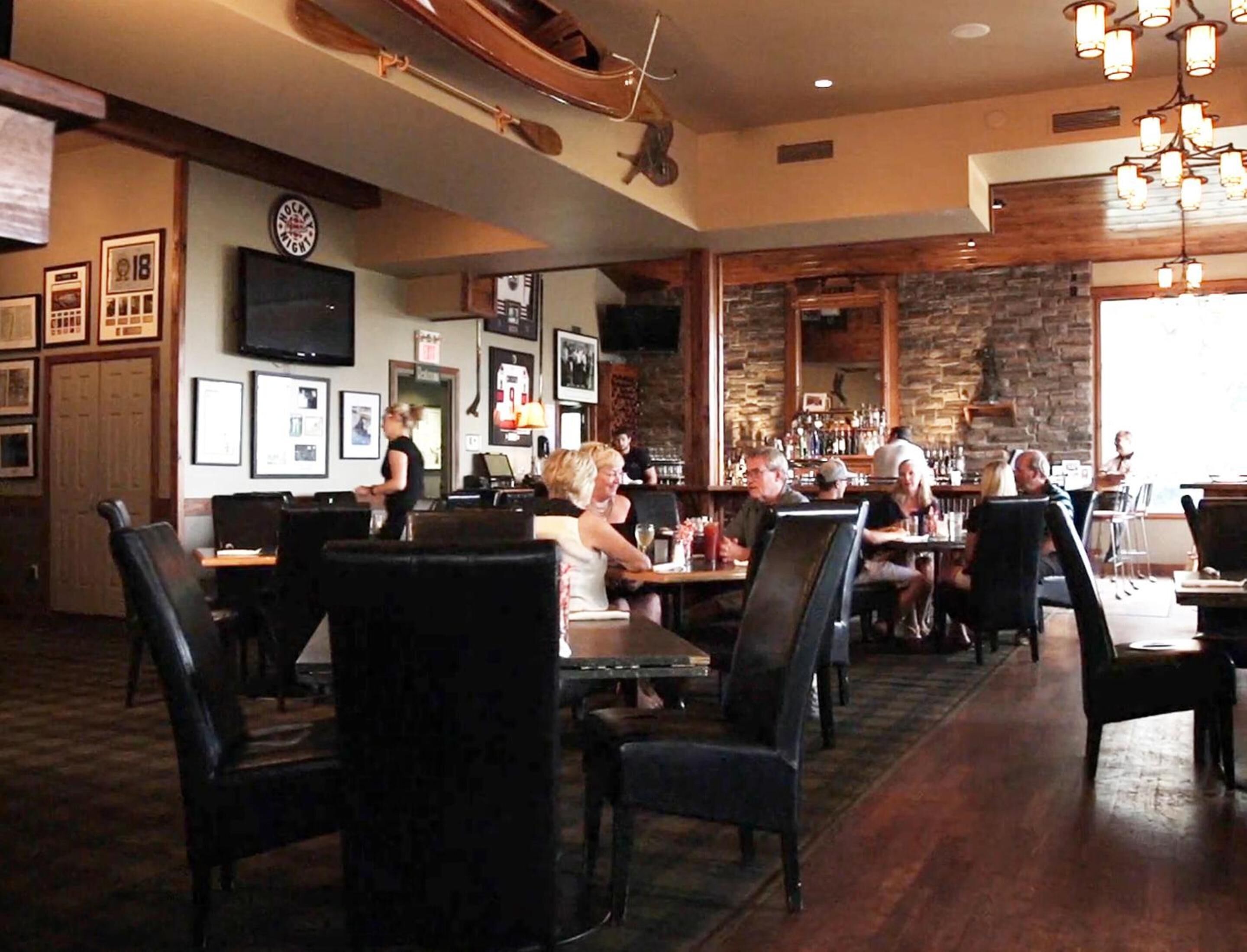 A restaurant with wooden flooring, black upholstered chairs, and a stone wall.