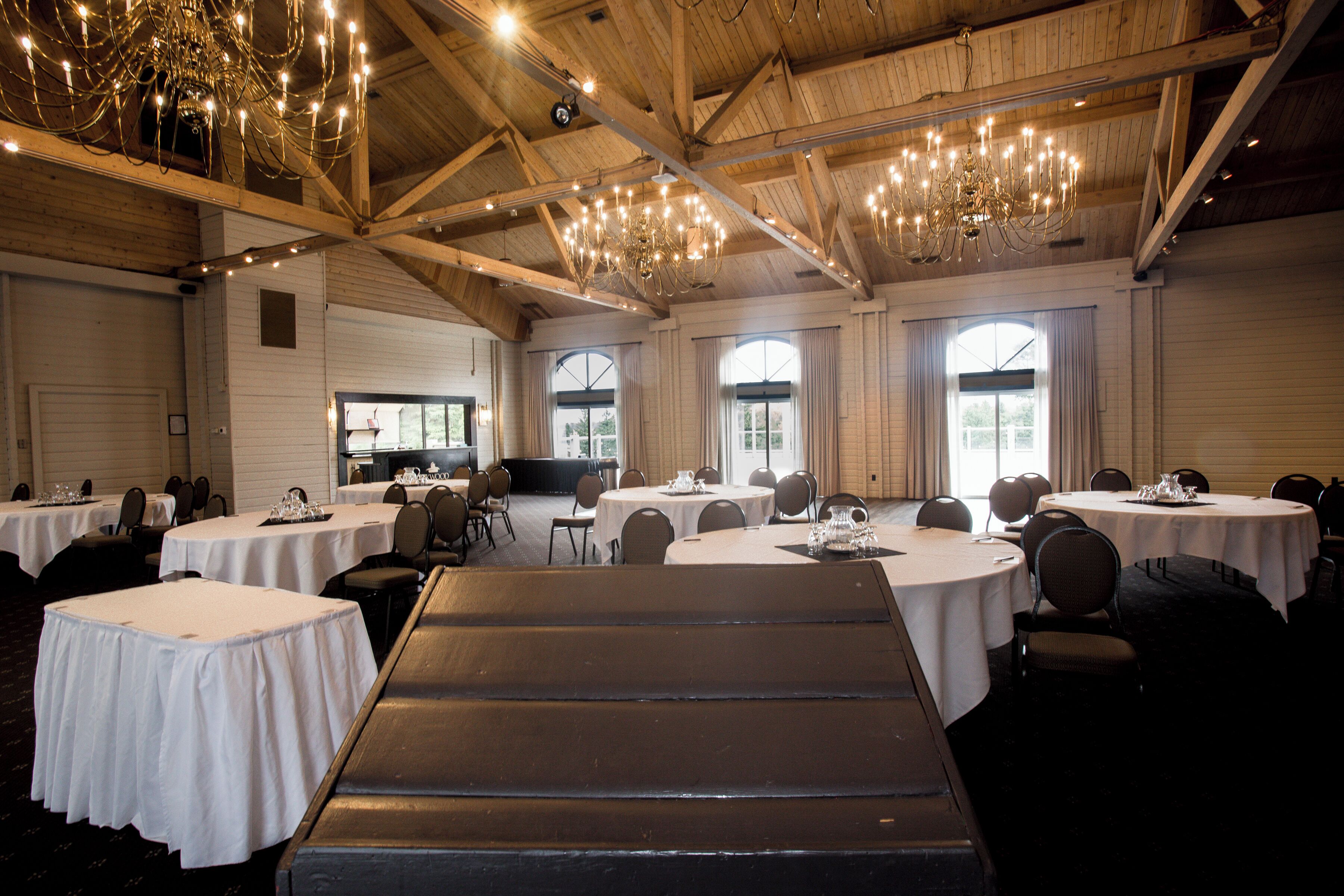 A banquet hall with round tables, chairs, and a stage area.