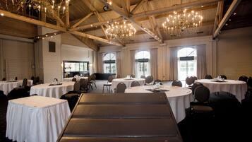A banquet hall with round tables, chairs, and a stage area.
