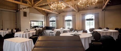 A banquet hall with round tables, chairs, and a stage area.