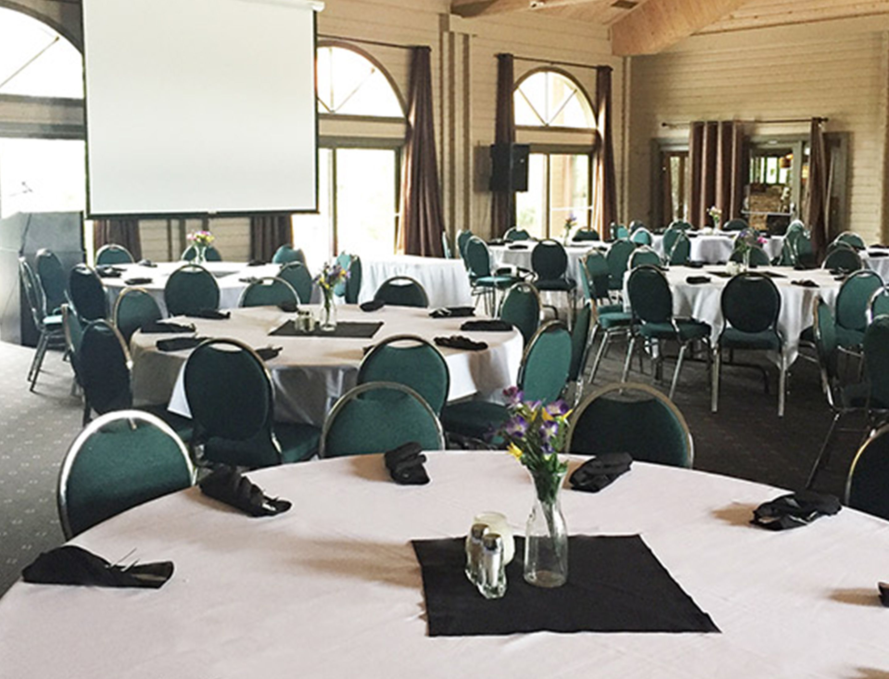 Une salle de conférence équipée de plusieurs tables, de chaises et d’un écran de projection.