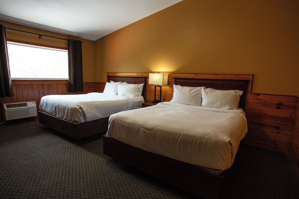 Quarto de hotel com duas camas, uma janela com cortinas, um aquecedor fixado na parede e um abajur.