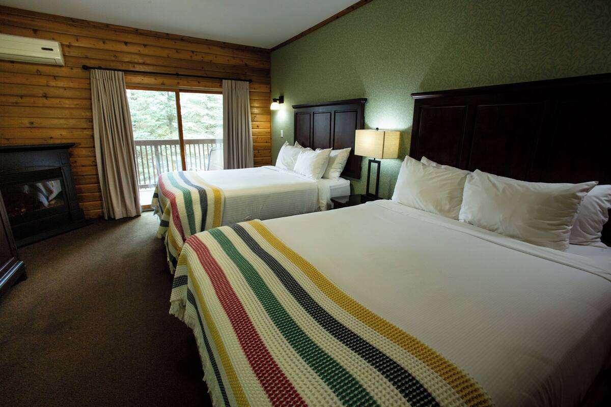 Quarto de hotel com duas camas, lareira e varanda com cortinas.