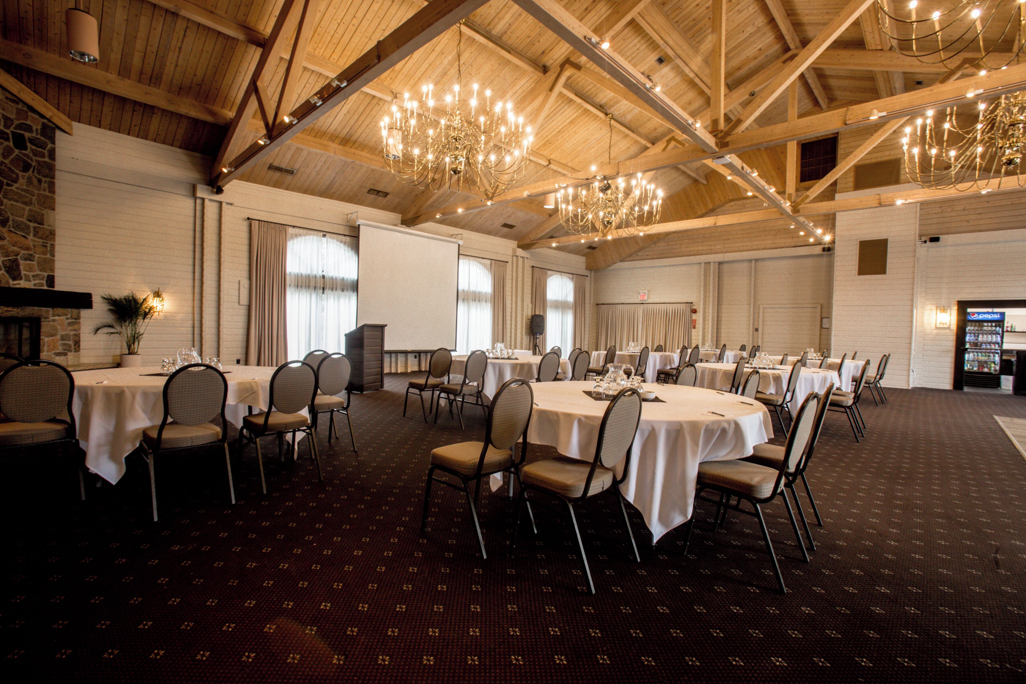 Un salón de banquetes con varias mesas redondas, sillas, candelabros y una pared de piedra.