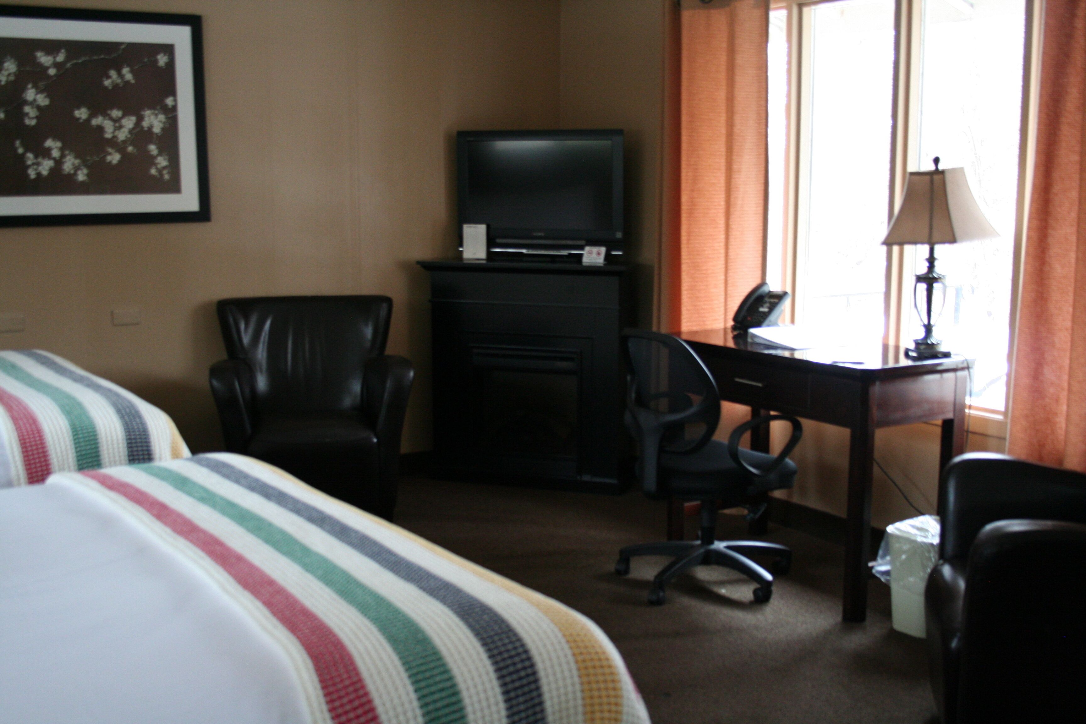 A hotel room with two beds, a television, a desk with a chair, and a lamp.