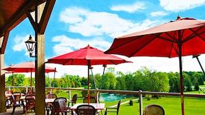 An outdoor patio with tables and chairs, red umbrellas, and a view of a green landscape. - Oakwood Resort (South Huron)