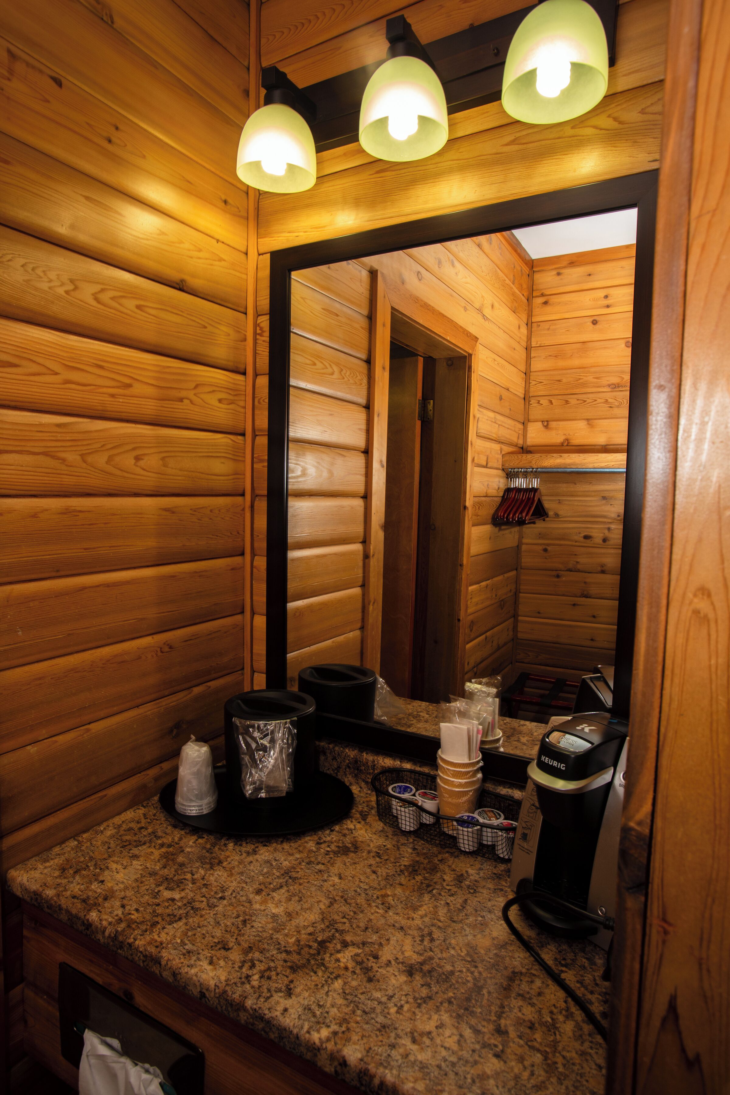 Un baño tipo cabaña de madera con encimera de granito, cafetera y espejo.