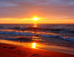 Een strand bij zonsondergang, met golven en een heldere lucht.