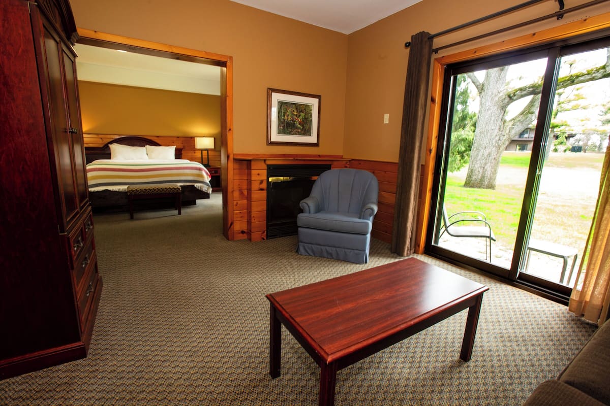 Quarto de hotel com cama, poltrona azul, mesa de madeira e lareira.