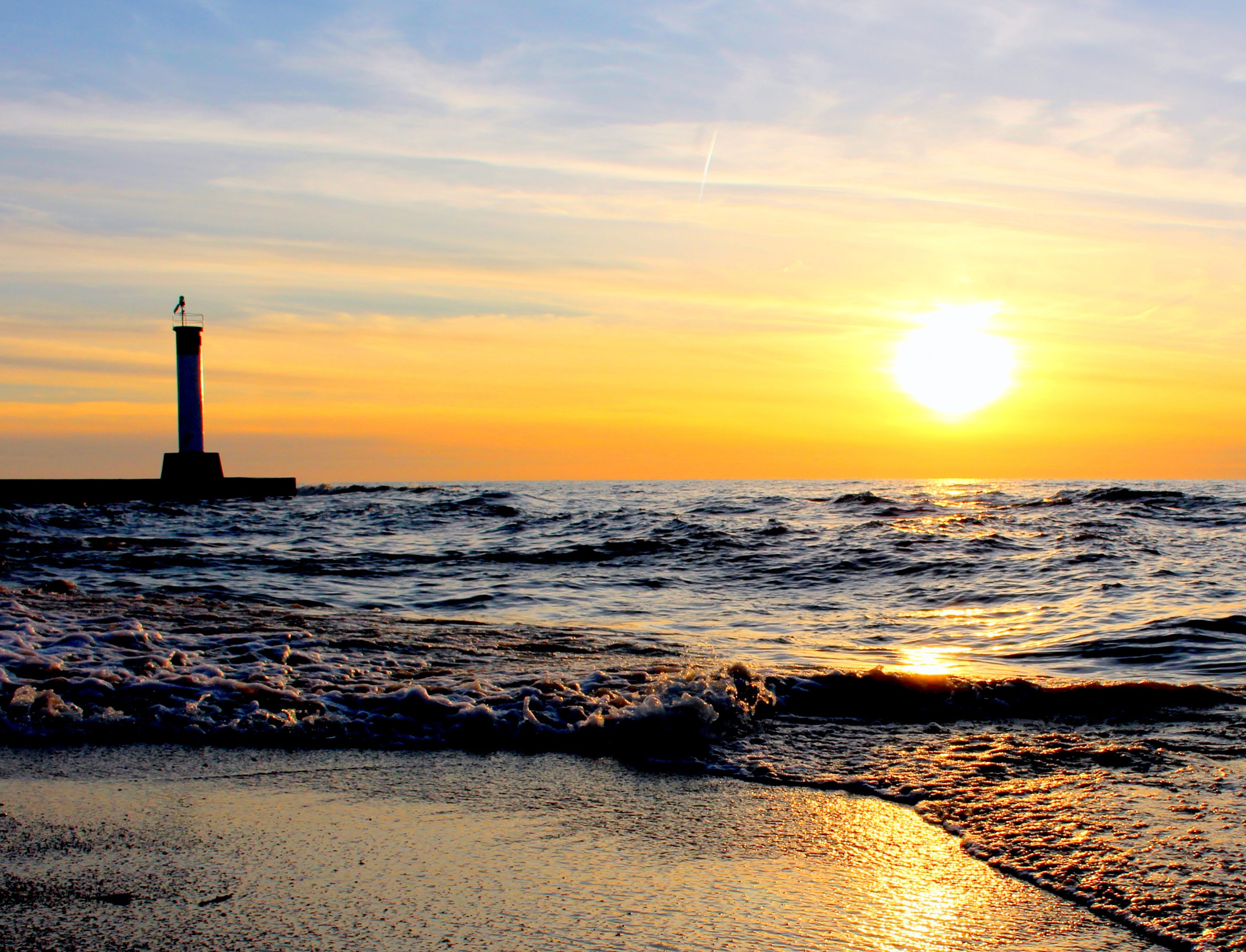 A lighthouse at sunset with waves crashing onto the shore.