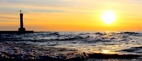 A lighthouse at sunset with waves crashing onto the shore.