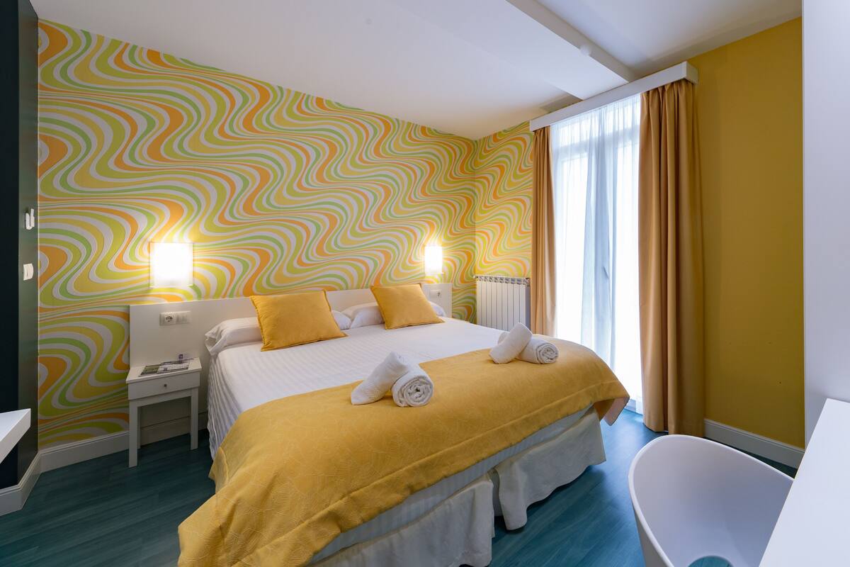 A hotel room with a bed, bedside tables, a chair, and a window with curtains.