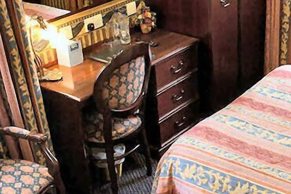 A bedroom with a bed, a wooden dresser, a chair, and a desk with a mirror.