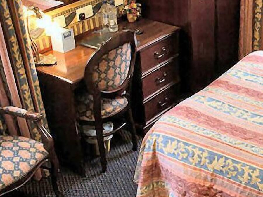 A bedroom with a bed, a wooden dresser, a chair, and a desk with a mirror.