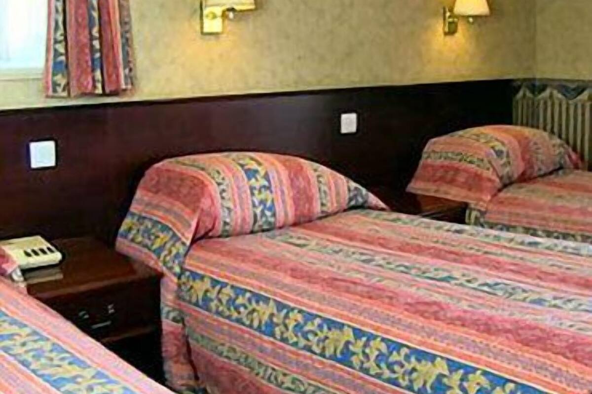 A hotel room with two beds, each with patterned bedding, bedside lamps, and a small table with a telephone.