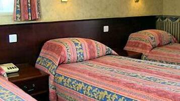 Ett hotellrum med två sängar, där varje säng har mönstrat sänglinne, sänglampor och ett litet bord med en telefon.