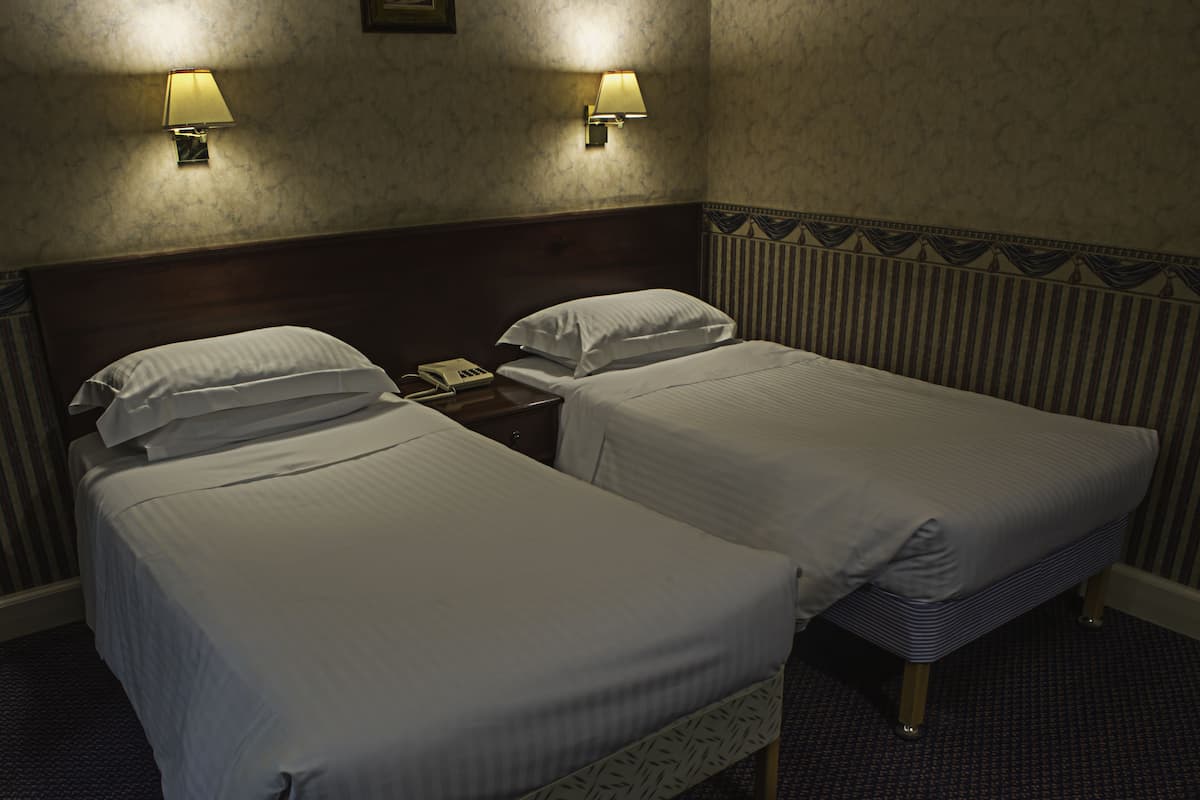 A hotel room with two beds, a nightstand with a phone, and two wall-mounted lamps.