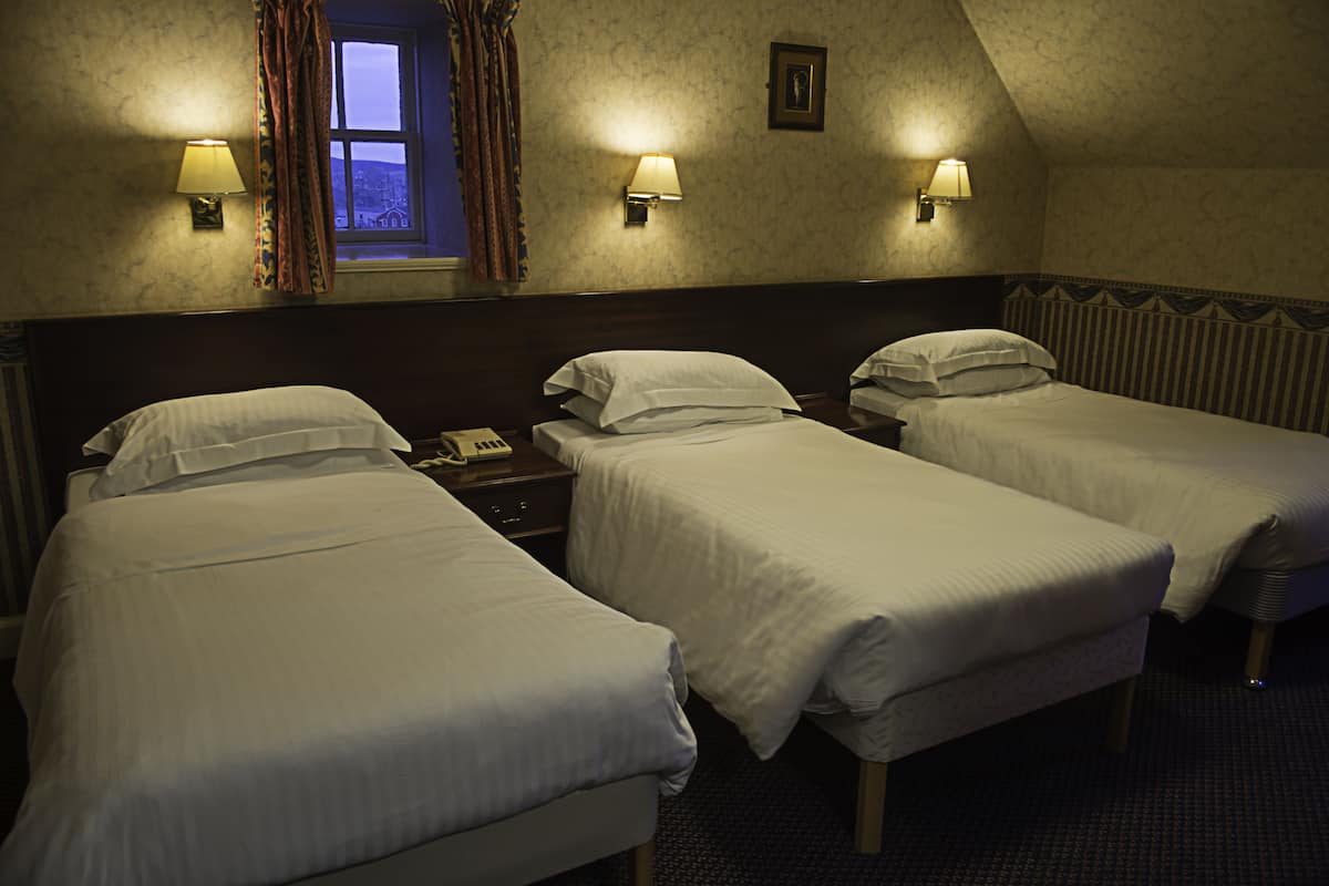A hotel room with three single beds, a nightstand with a telephone, and two wall-mounted lamps.