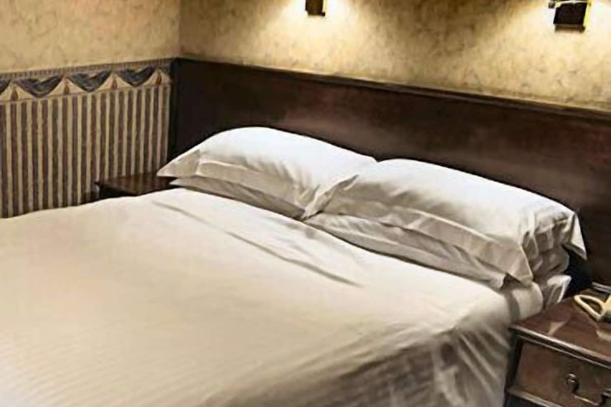 A neatly made bed with white linens, a wooden headboard, and a nightstand with a telephone.