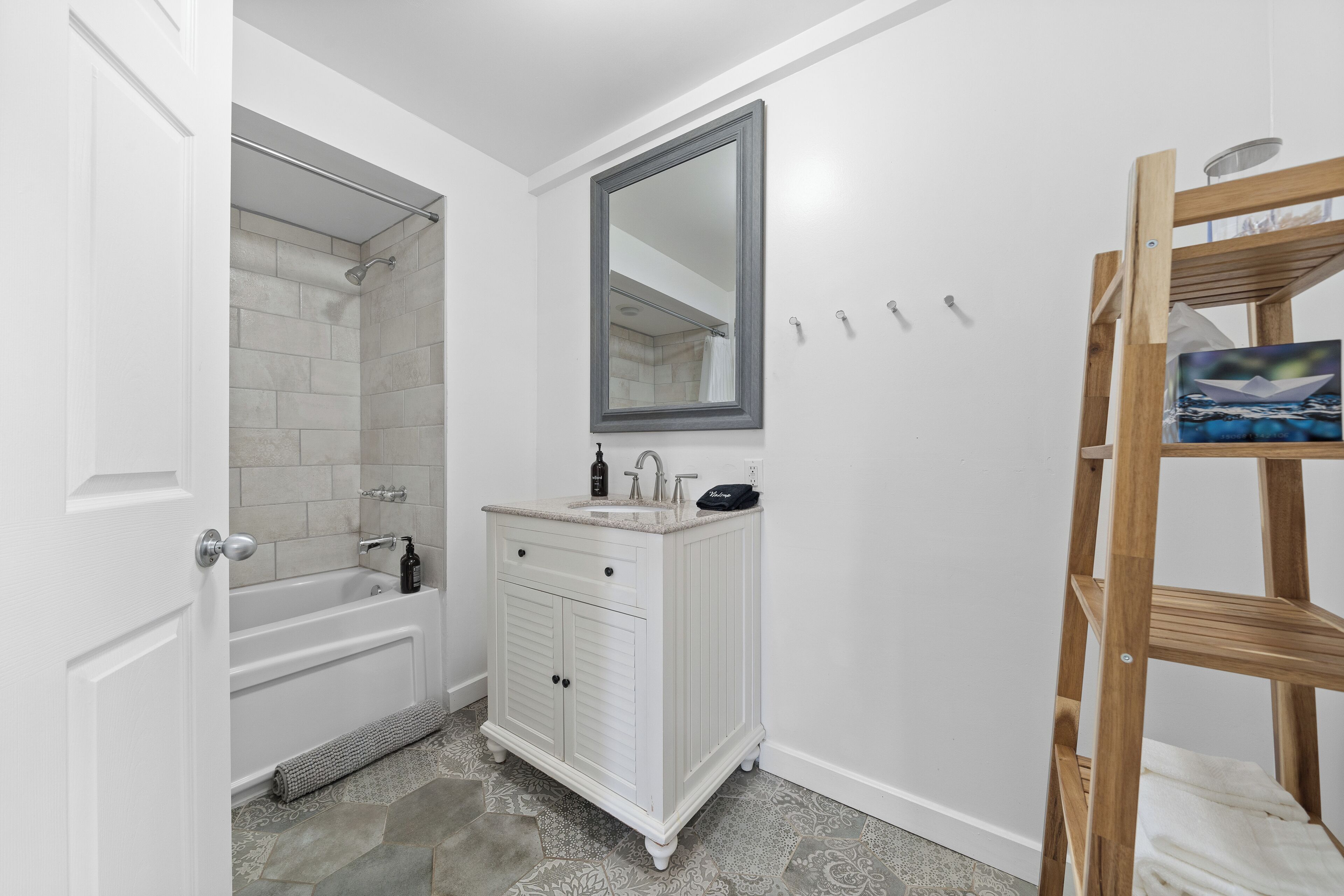 A bathroom with a white vanity, a shower, and a wooden shelf.