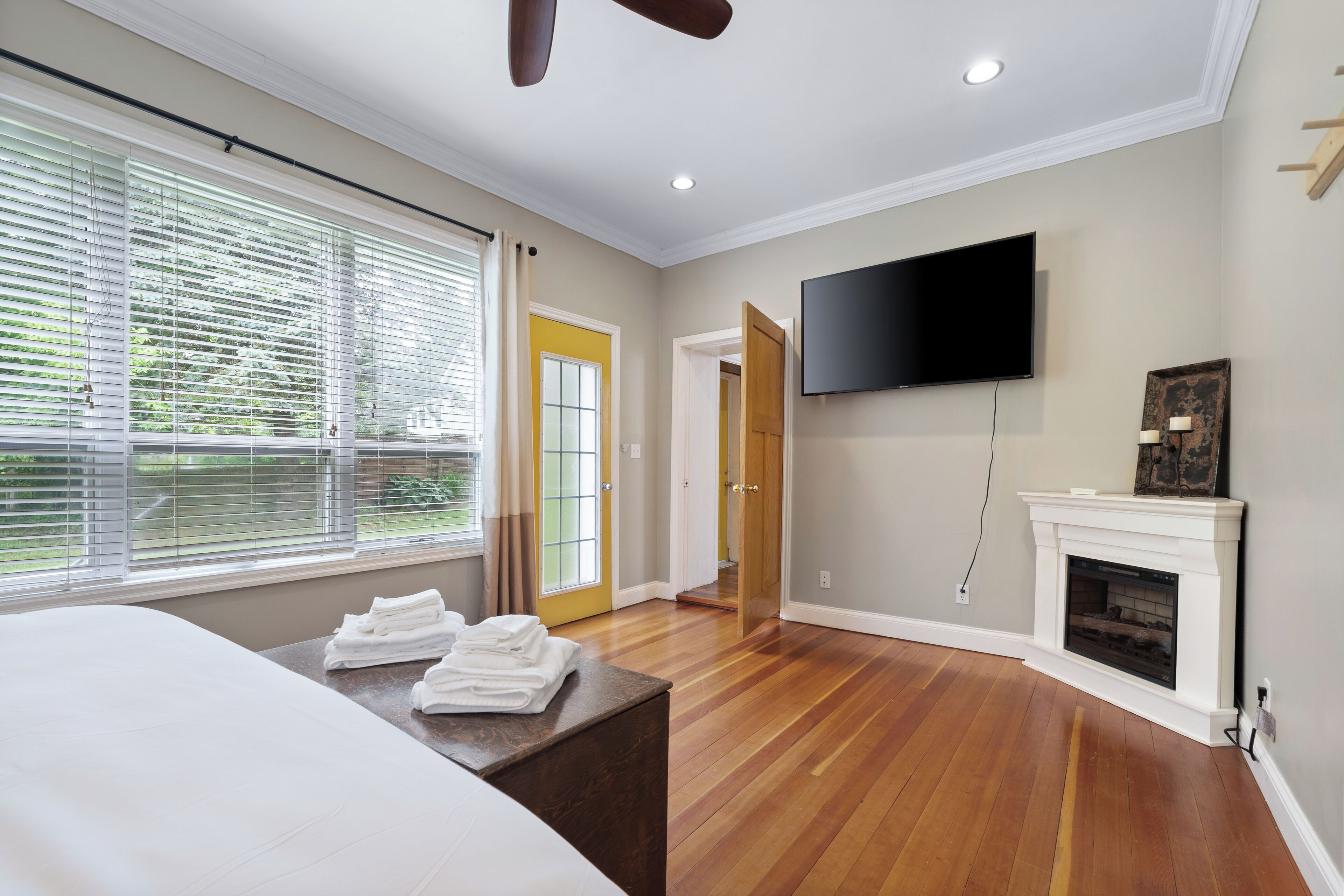 A modern bedroom with a large bed, a flat-screen TV, a fireplace, and a view of the outdoors through large windows.