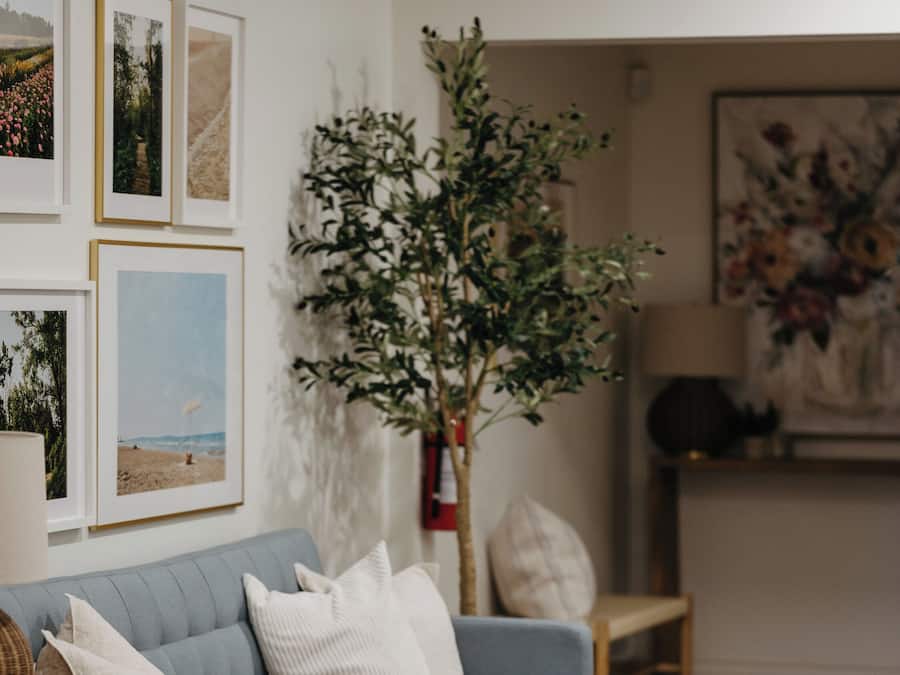 A living room with a grey sofa, a wooden side table, a white rug, and framed pictures on the wall.