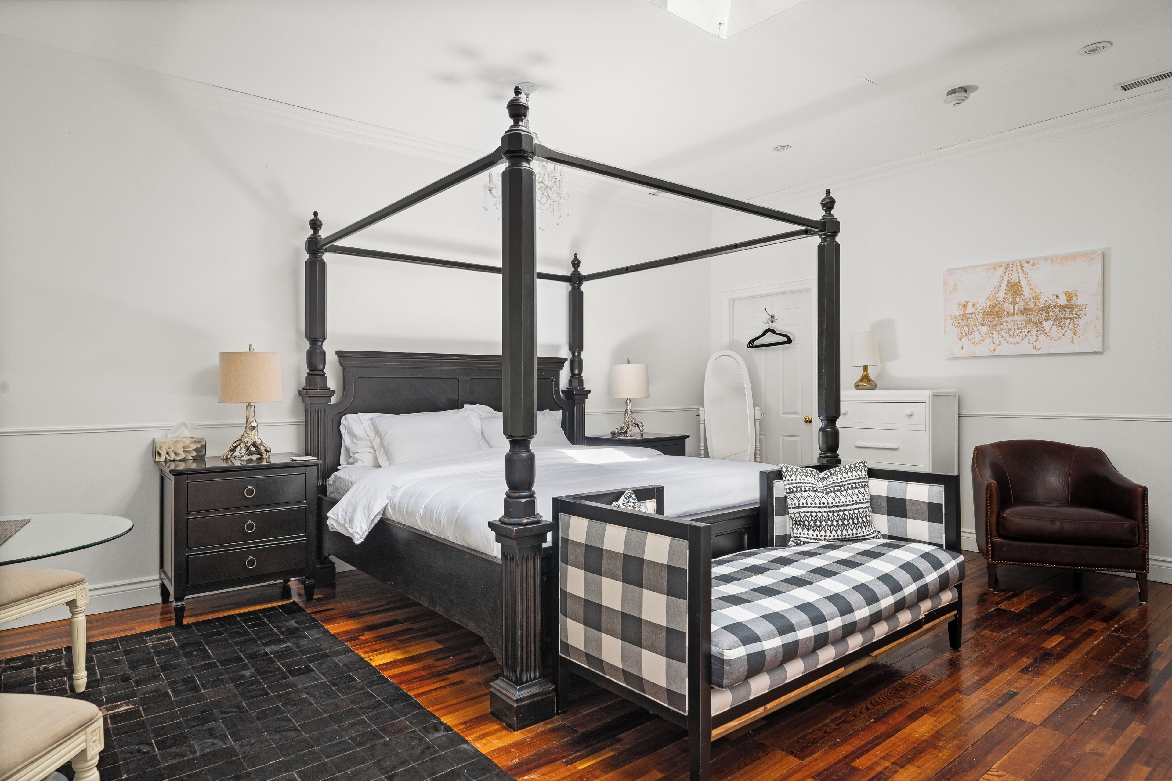 A four-poster bed with a checkered bench, bedside tables with lamps, a chair, and a view of the city skyline.