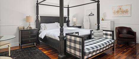 A four-poster bed with a checkered bench, bedside tables with lamps, a chair, and a view of the city skyline.