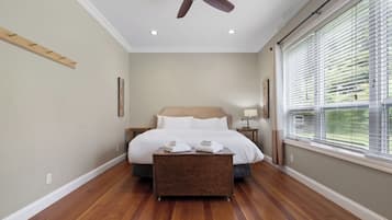 Un dormitorio con cama, ventilador de techo, mesita de noche y ventana con persianas.
