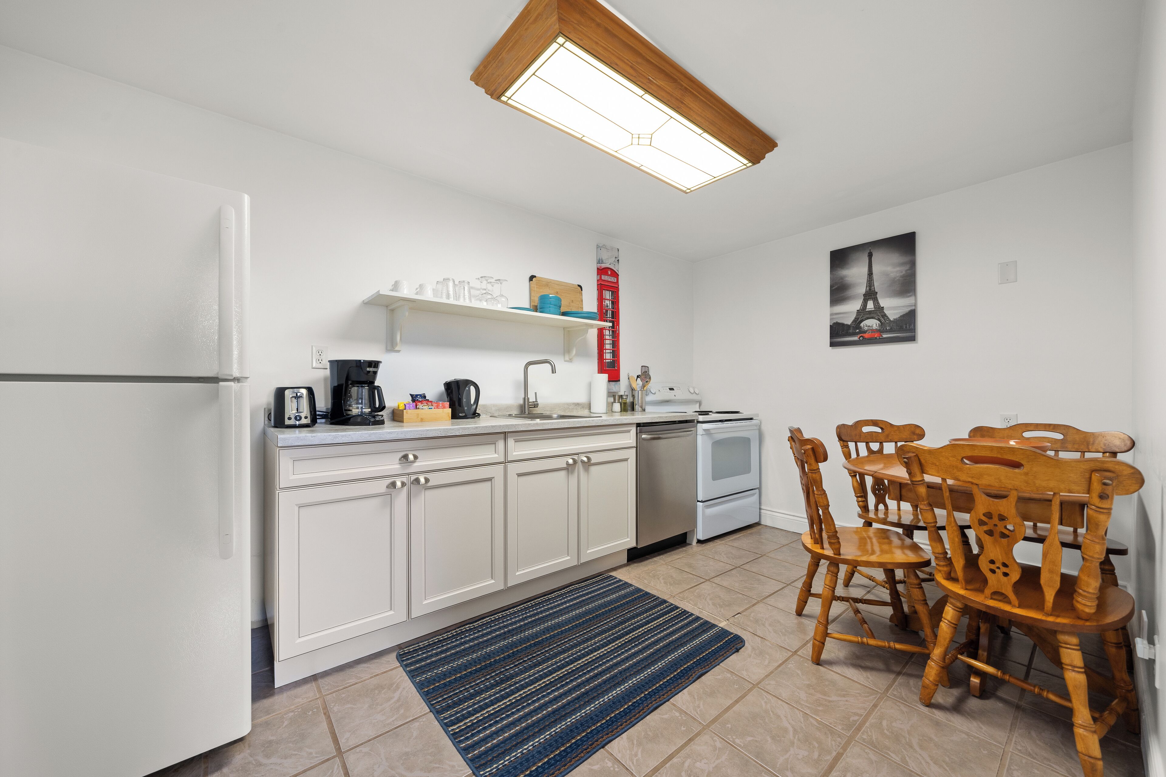 A compact kitchen with white cabinets, a built-in oven, a coffee maker, and a dining table with wooden chairs.