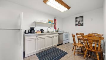 A compact kitchen with white cabinets, a built-in oven, a coffee maker, and a dining table with wooden chairs.