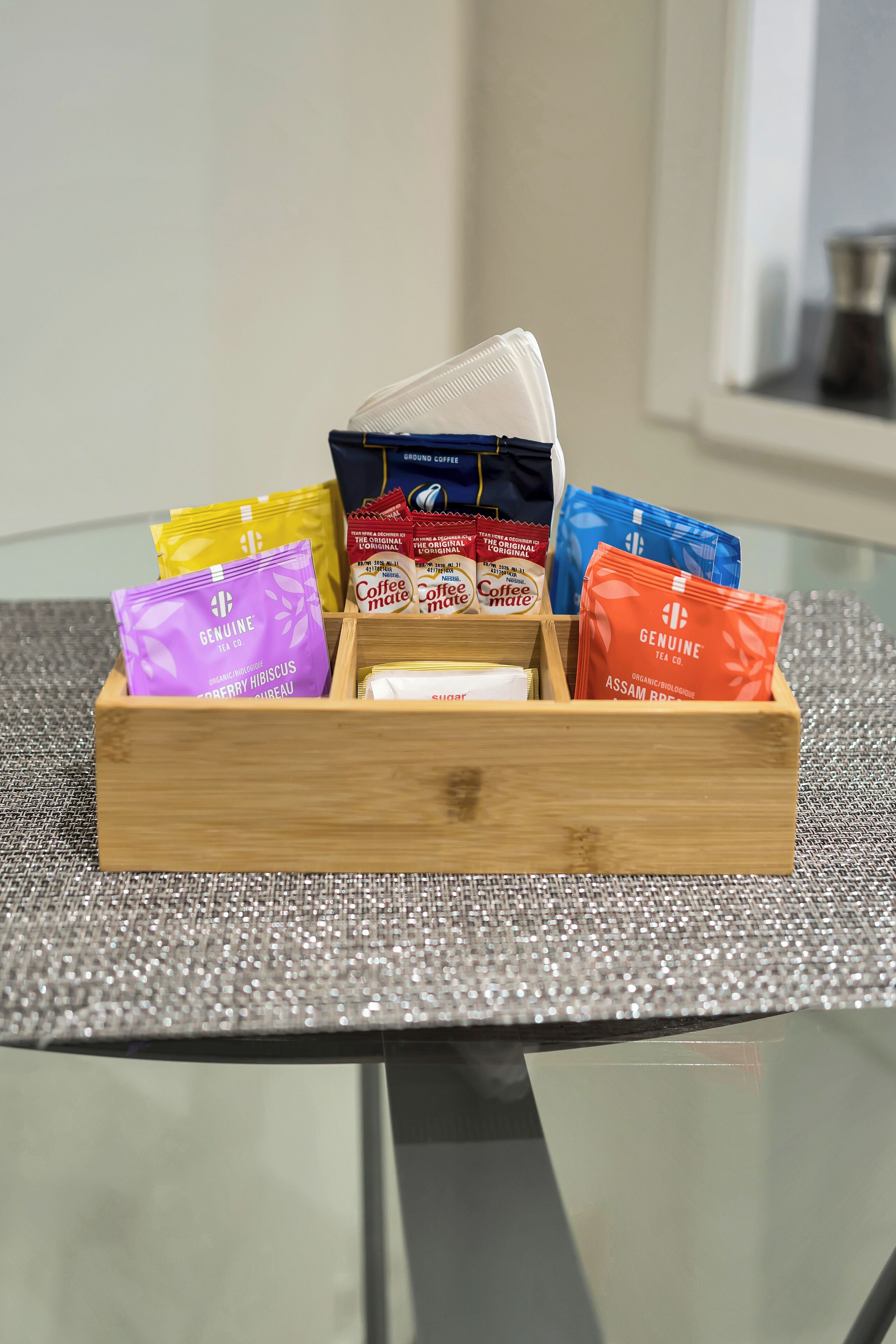 A wooden box containing various tea bags on a glass table with a textured placemat.