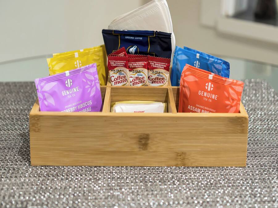A wooden box containing various tea bags on a glass table with a textured placemat.