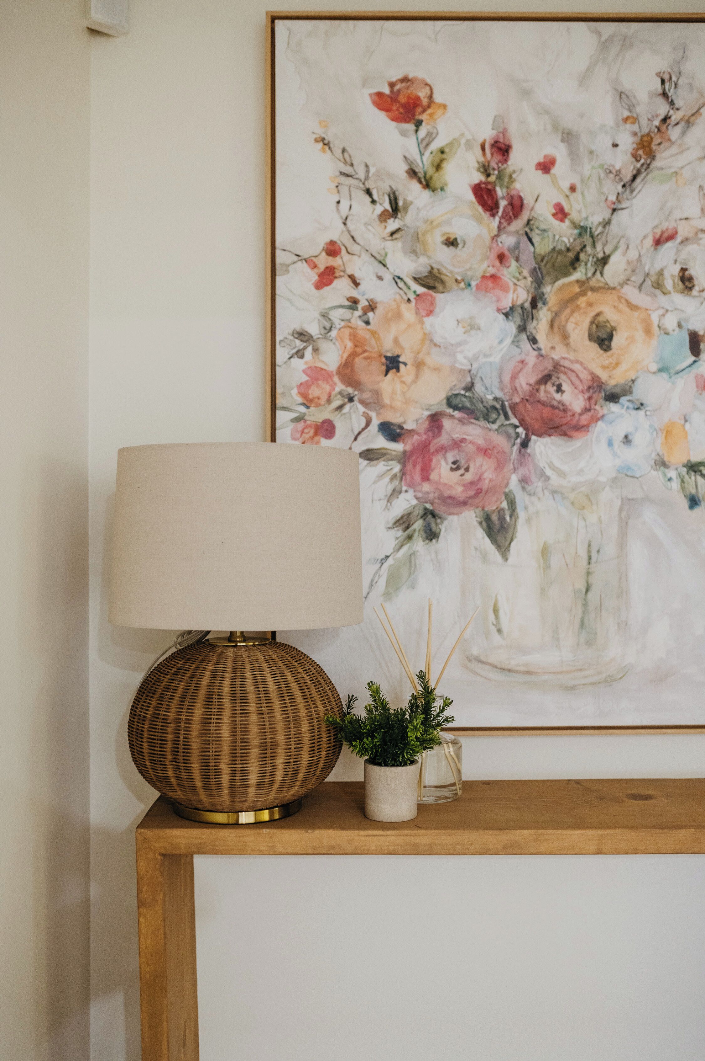 A table with a lamp, a small potted plant, and a framed floral painting.