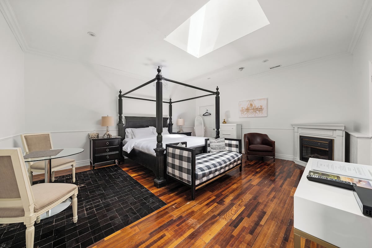 Un dormitorio con una cama con dosel, un escritorio con silla, una chimenea y un tragaluz.