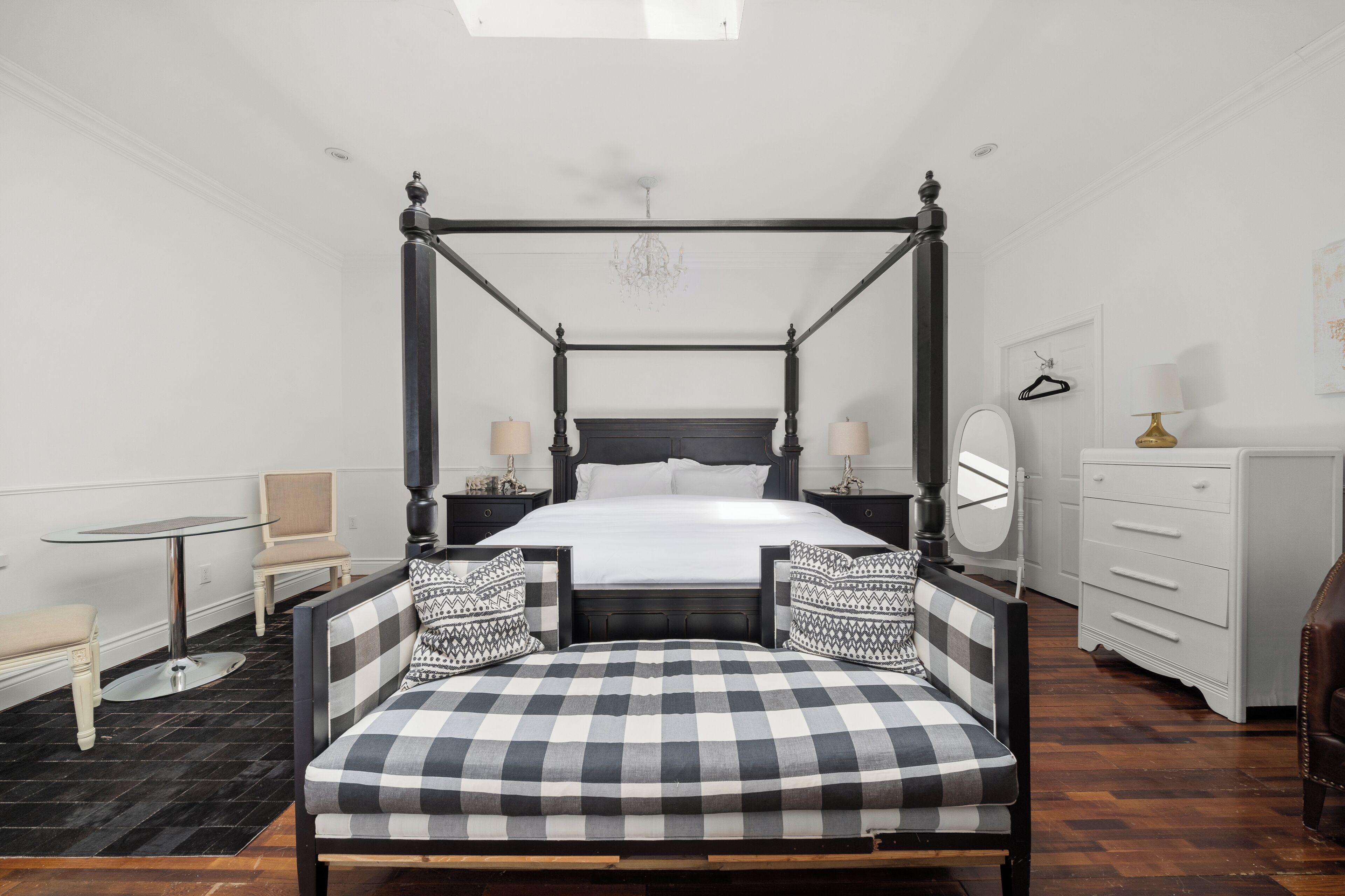 A four-poster bed with a checkered upholstered bench, a bedside table, a mirror, and a dresser in a hotel room.