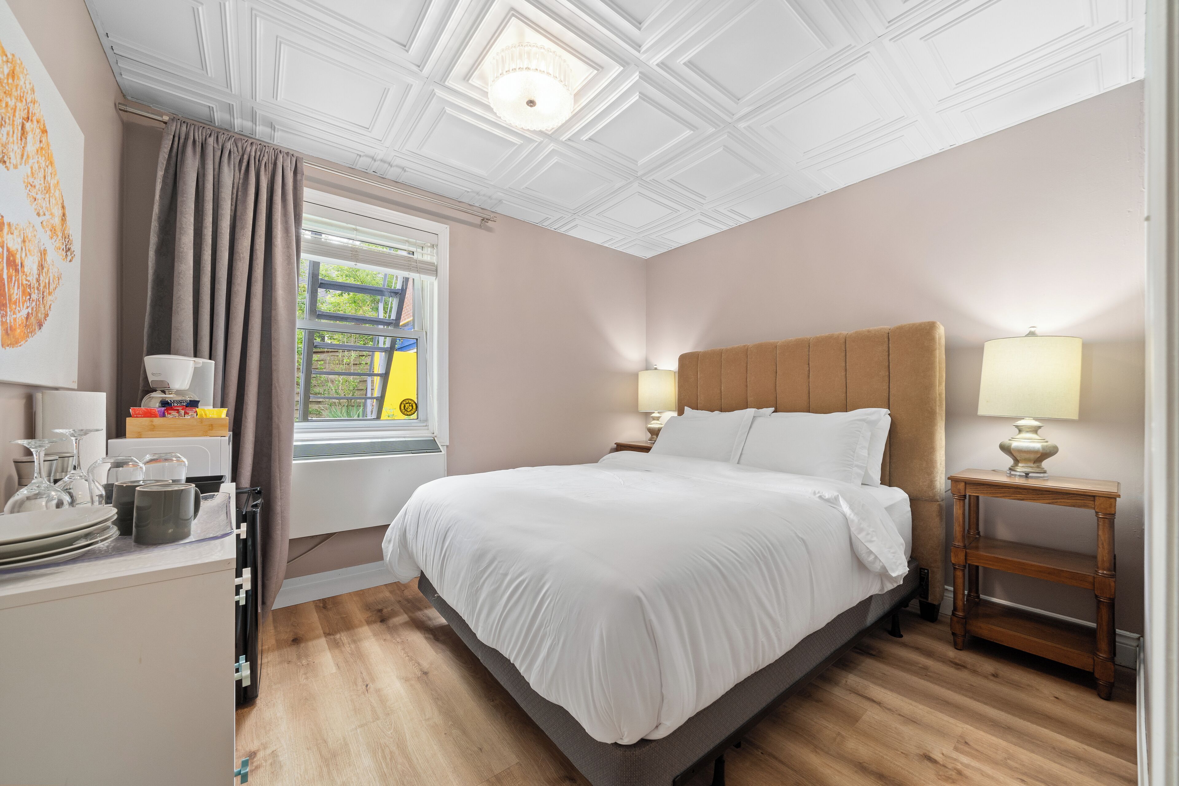 A neatly arranged bedroom with a large bed, bedside lamps, a wooden nightstand, and a window with curtains.