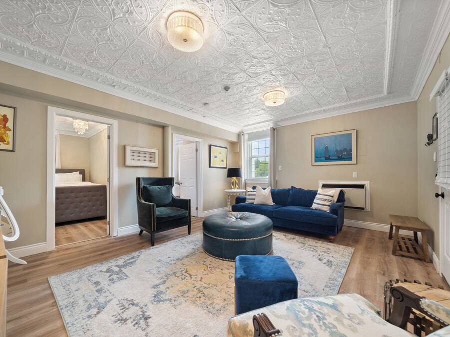 A spacious living room with a high ceiling, a blue sofa set, a wooden coffee table, and a patterned rug.
