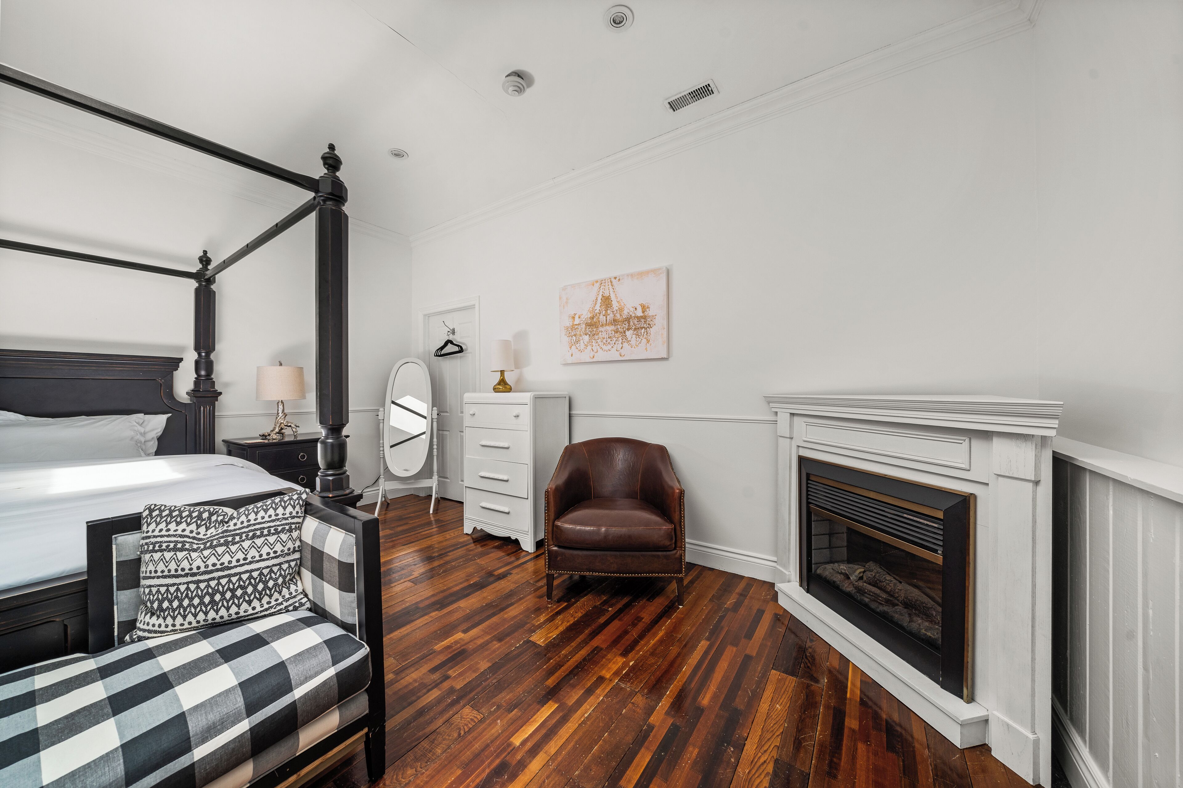 A bedroom with a four-poster bed, a fireplace, a chair, and a dresser.
